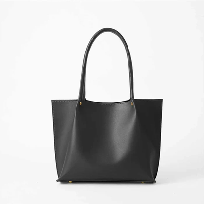 Black leather tote bag with long handles on a white background.