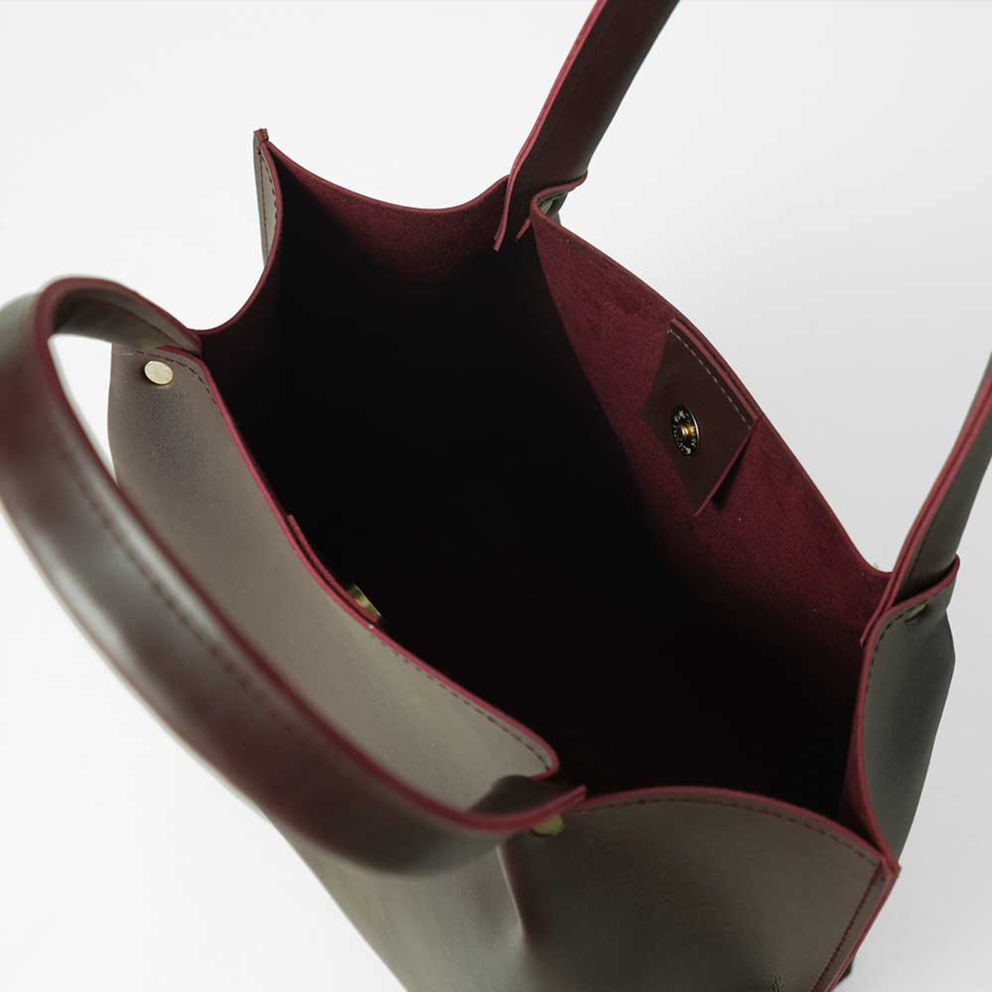 Close-up of a maroon leather handbag with visible stitching on a white background